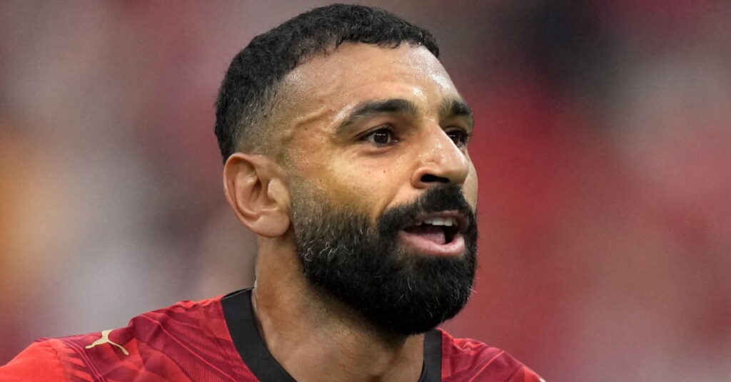 Den egyptiske fotballspilleren Mohamed Salah ser til venstre med åpen munn mens han var på en fotballstadion under FIFA fotball-VM 2026 og iført en rød landslagsfotballskjorte med svart kant